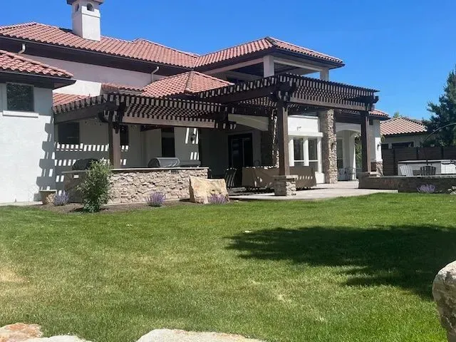 Large Mediterranean-style house with a stone patio, green lawn, and clear blue sky.