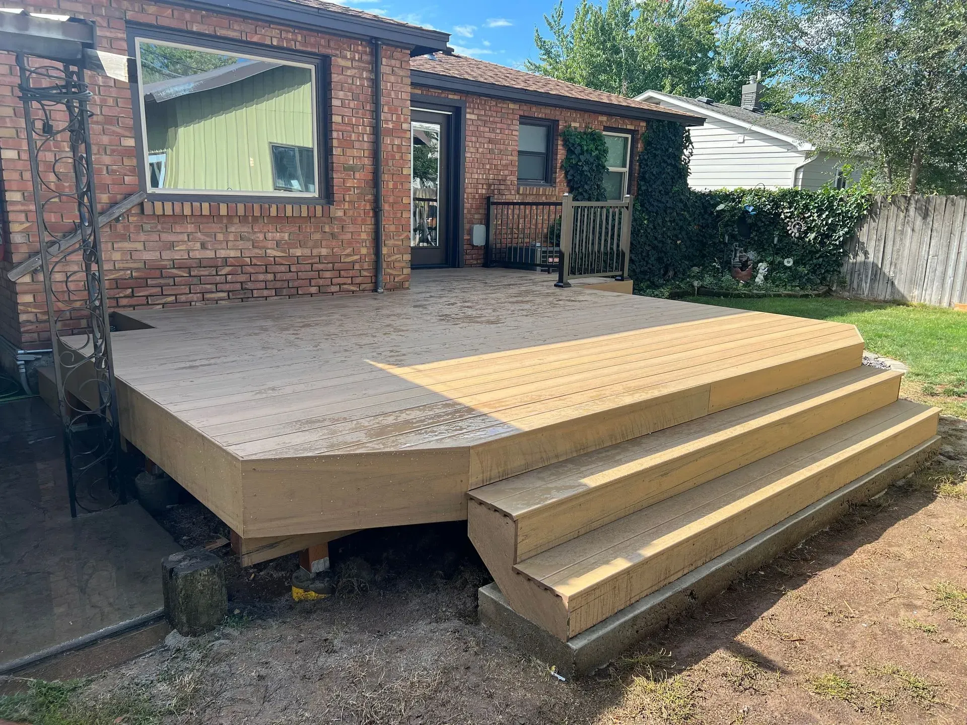 Backyard wooden deck with steps beside a brick house, under construction.