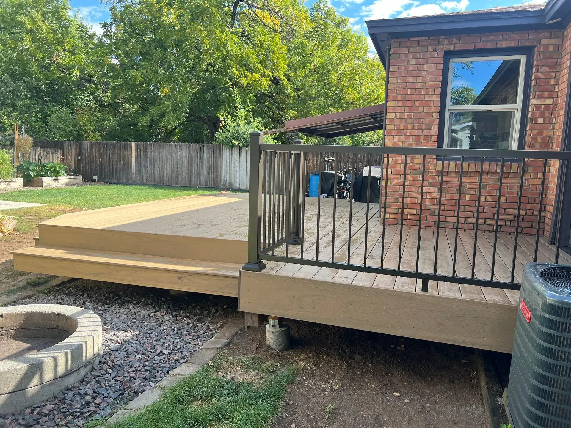 Backyard deck beside brick house with black railing and raised platform over gravel and fire pit.