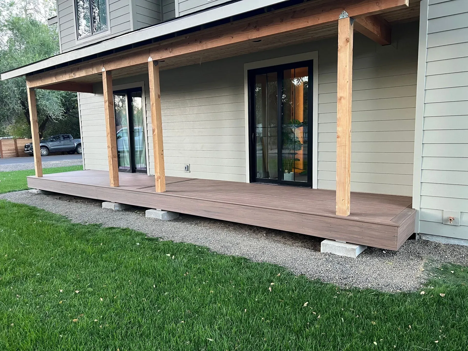Covered wooden porch with posts and sliding glass door on a house, beside a grassy yard