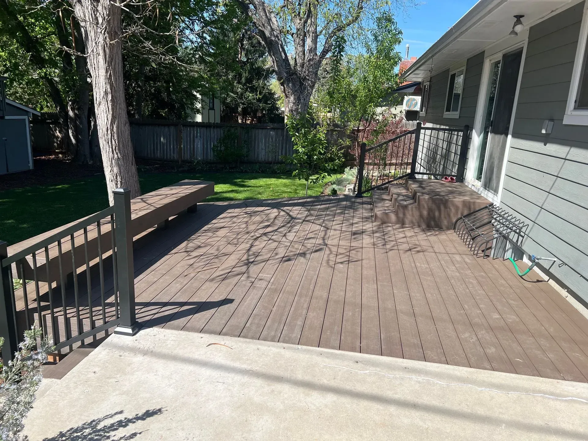 Backyard wooden deck with railings, steps, and house siding in sunlight