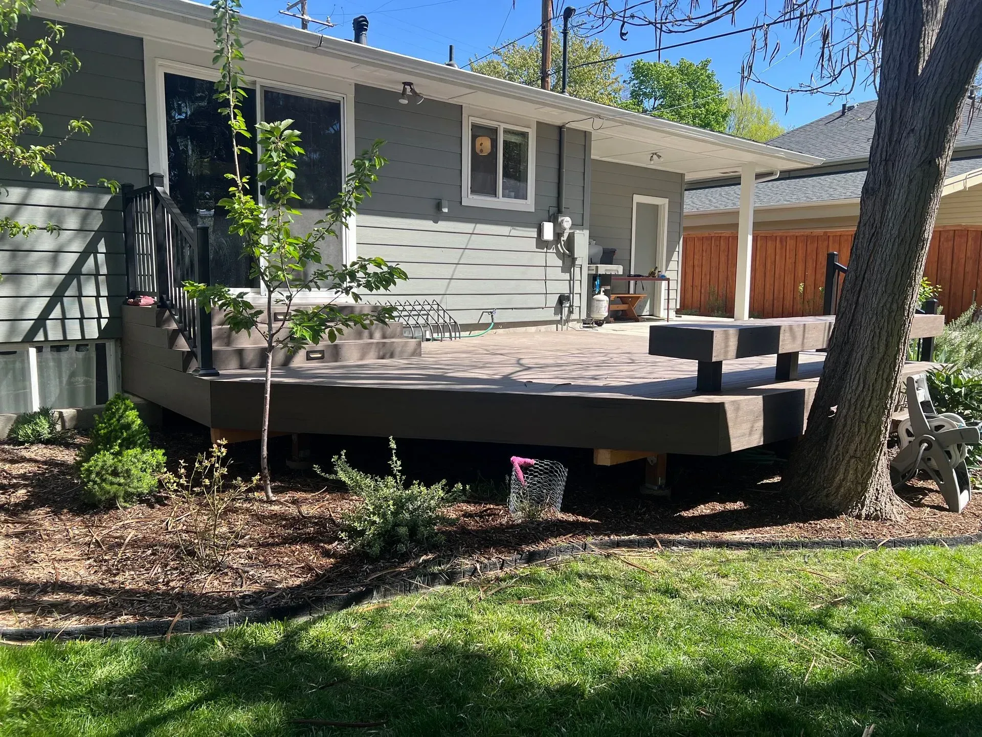 Backyard wooden deck attached to a gray house, with stairs, trees, and a grassy yard