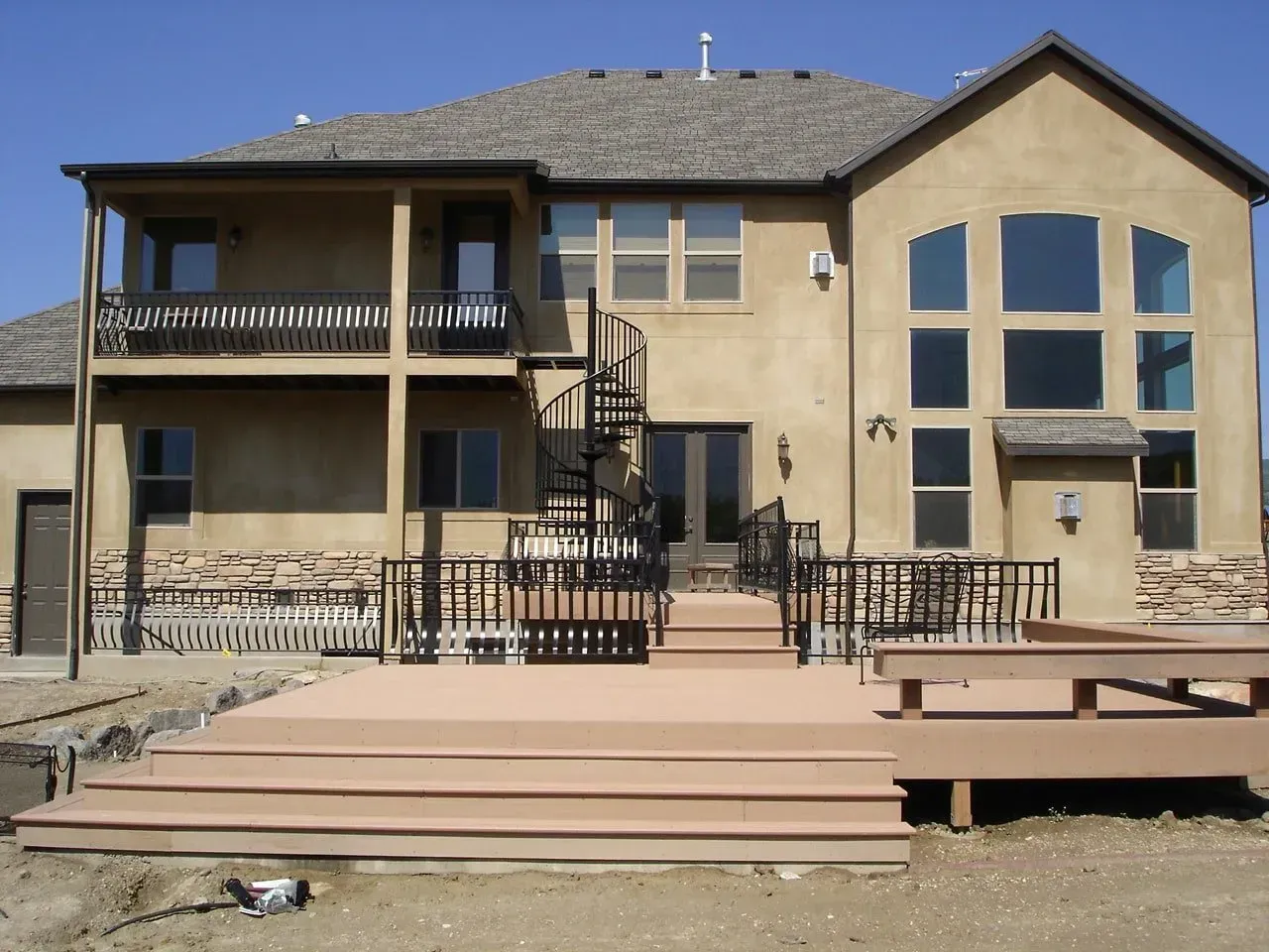Two-story beige house with raised wooden deck, stairs, and railing in a backyard setting