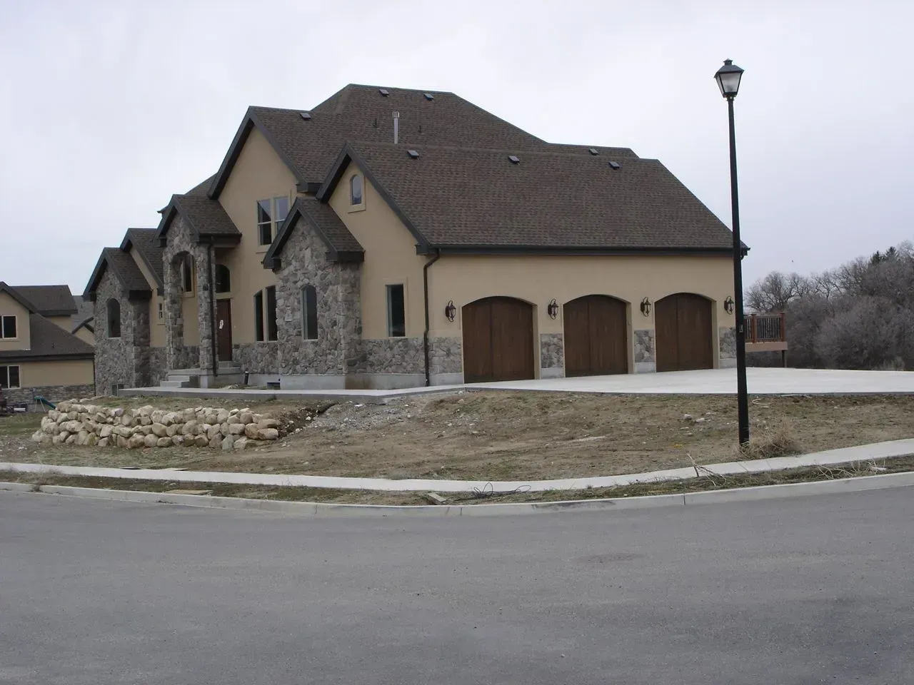 Suburban house with stone facade, two-car garage, and a streetlamp on a cloudy day