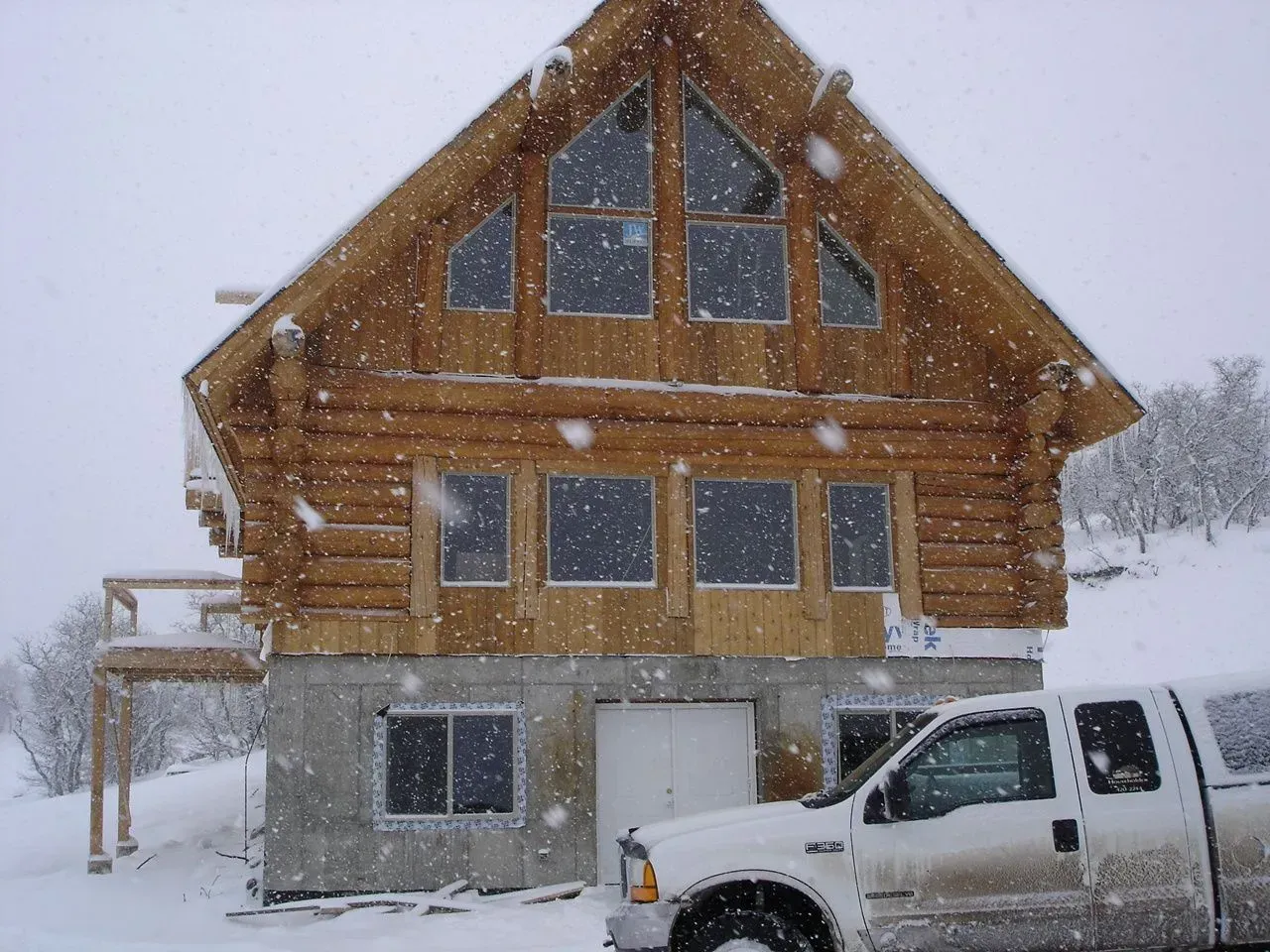 Snow-covered log cabin with a white truck parked outside during heavy snowfall