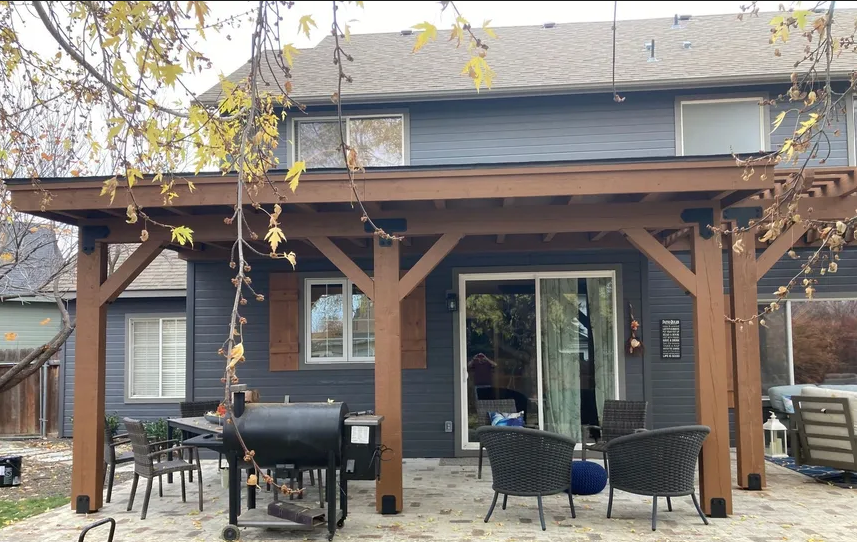 Backyard patio with wooden pergola, grill, outdoor seating, and sliding glass doors on a house