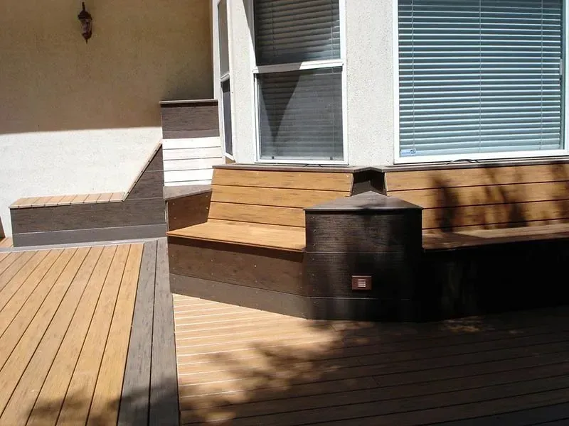 Backyard deck with wooden steps, white siding, and a black planter in sunlight