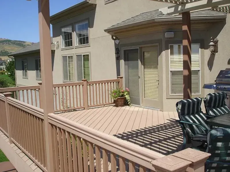 Wooden deck with railing beside a beige house, overlooking mountains in bright daylight