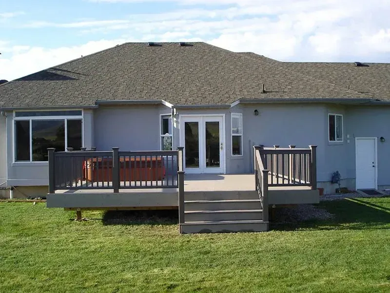 Single-story house with a wooden deck and stairs leading to a green lawn.