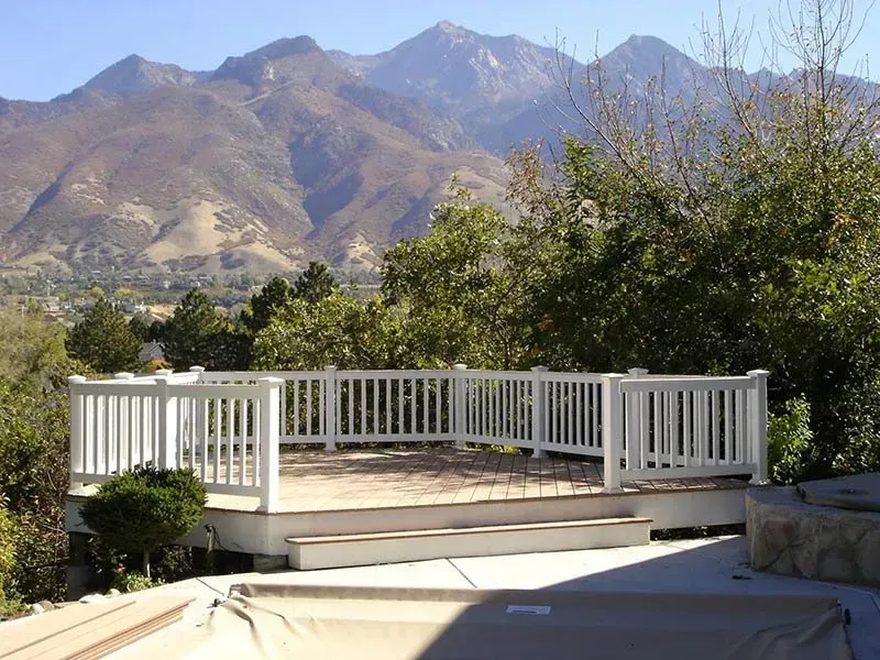 White deck with railing overlooking mountains and trees in a sunny outdoor landscape