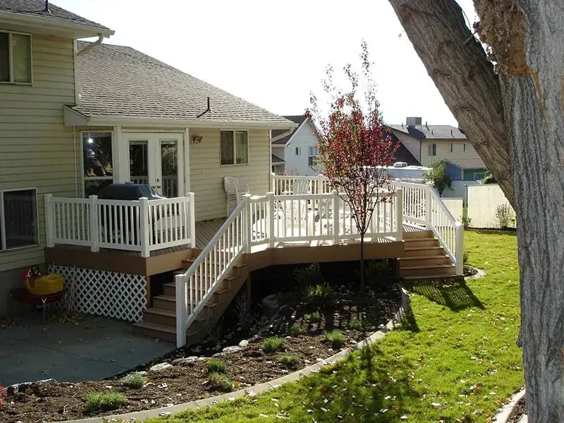 House deck with white railings and stairs, landscaped backyard, and a large tree in the foreground.