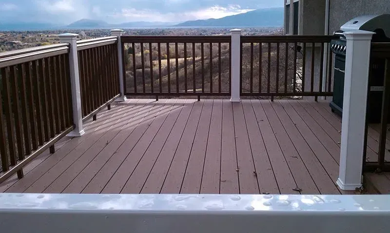 Wooden deck with railing overlooking a distant landscape and mountains under a cloudy sky