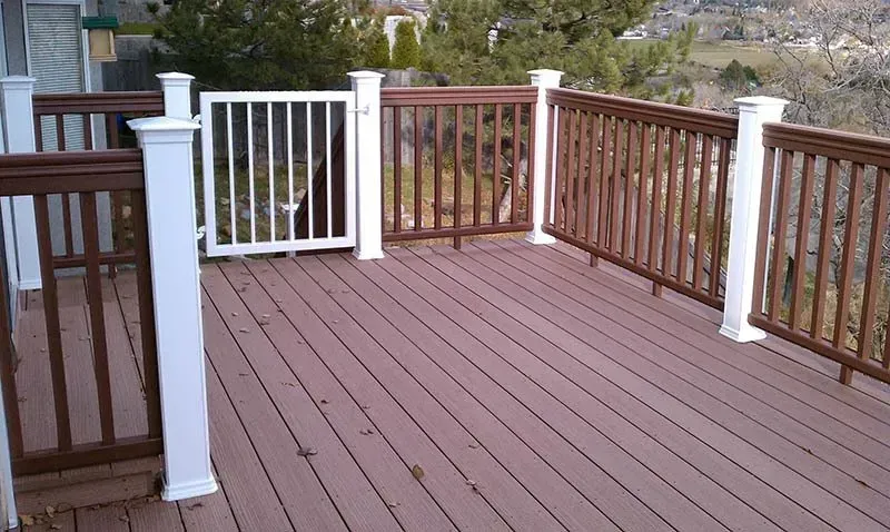 Wooden deck with brown railing, white posts, and a gate overlooking a yard and trees.