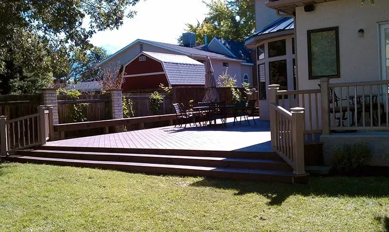 Wooden deck and steps beside a house, overlooking a grassy yard with a red barn in the background.