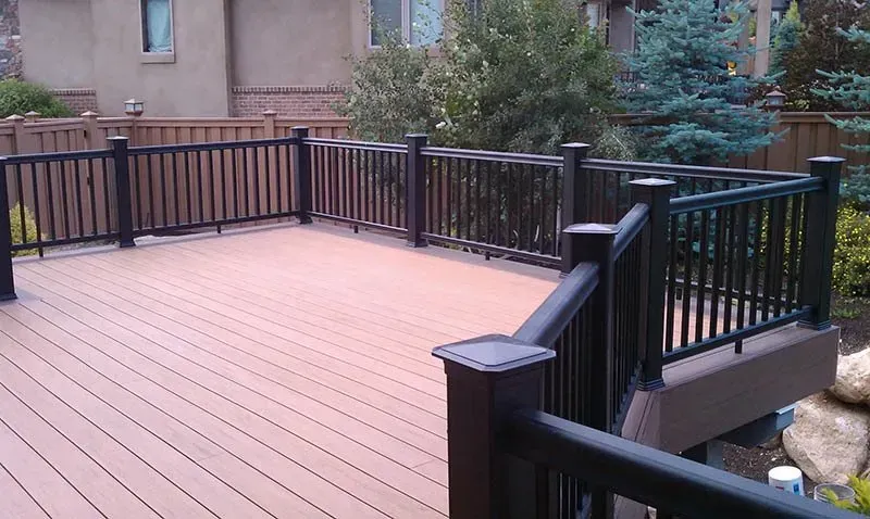 Wooden deck with black railing beside a house, overlooking a landscaped yard.
