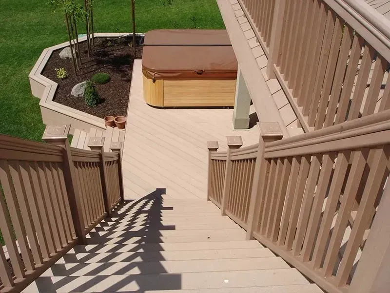 Wooden staircase leading to a deck with a hot tub and landscaped yard.
