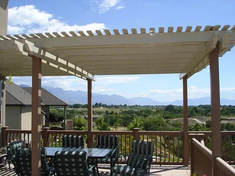 Patio with pergola, table and chairs, overlooking green landscape and distant mountains under a blue sky