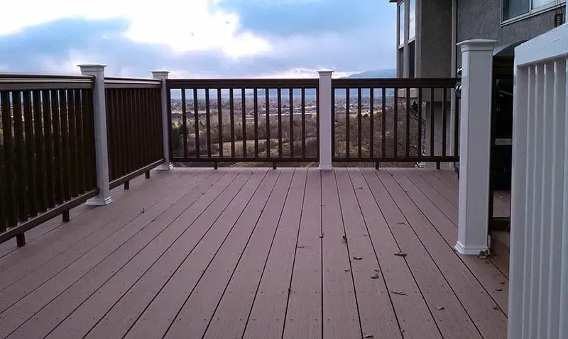 Wooden deck with brown railing overlooking a distant landscape under a cloudy sky
