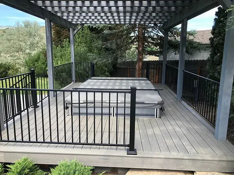 Outdoor wooden deck with black railing, pergola, and seating in a backyard garden