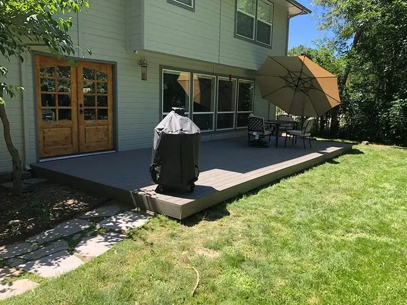 Backyard deck beside a house with patio furniture, grill, and umbrella in sunlight