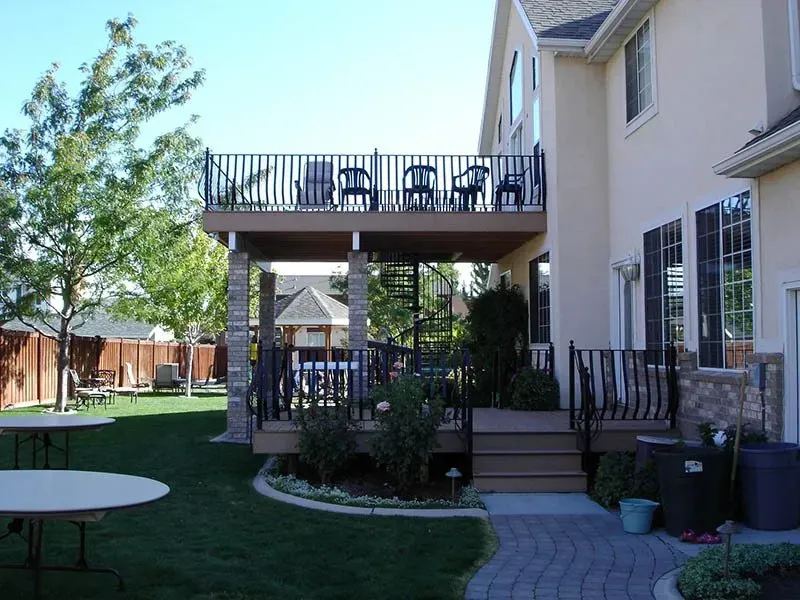 Backyard patio with raised deck, stairs, lawn, and patio furniture beside a house.