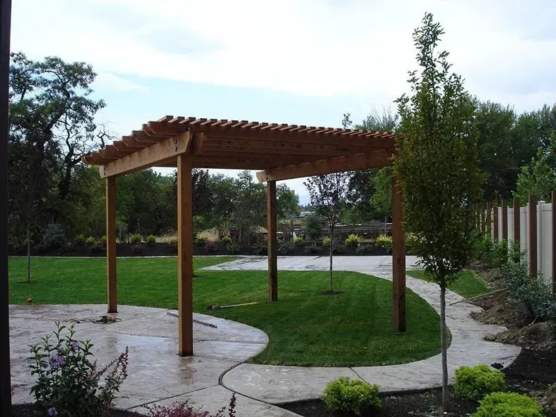 Wooden pergola in a landscaped garden with a curved stone patio and green lawn