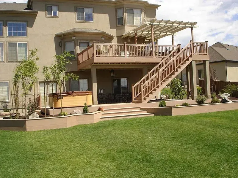 Backyard patio with wooden deck, stairs, pergola, and green lawn beside a house