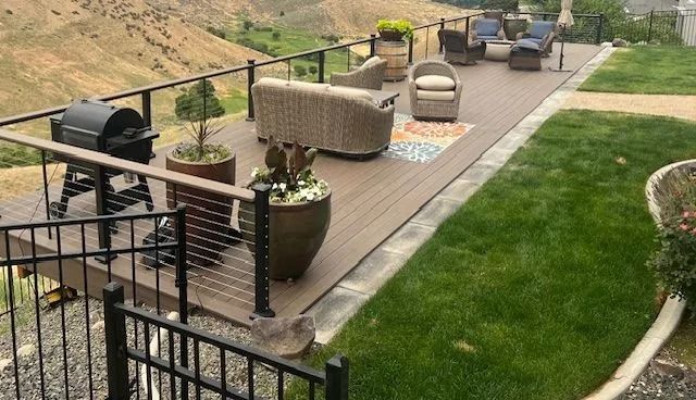 Backyard patio with outdoor seating, grill, potted plants, and green lawn beside a hillside