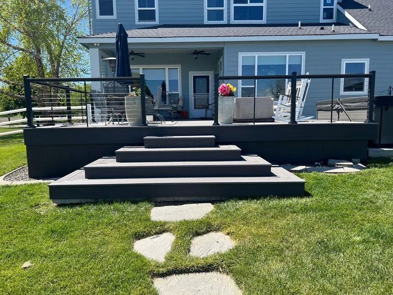 A dark gray deck with wide stairs leading to a grassy yard.