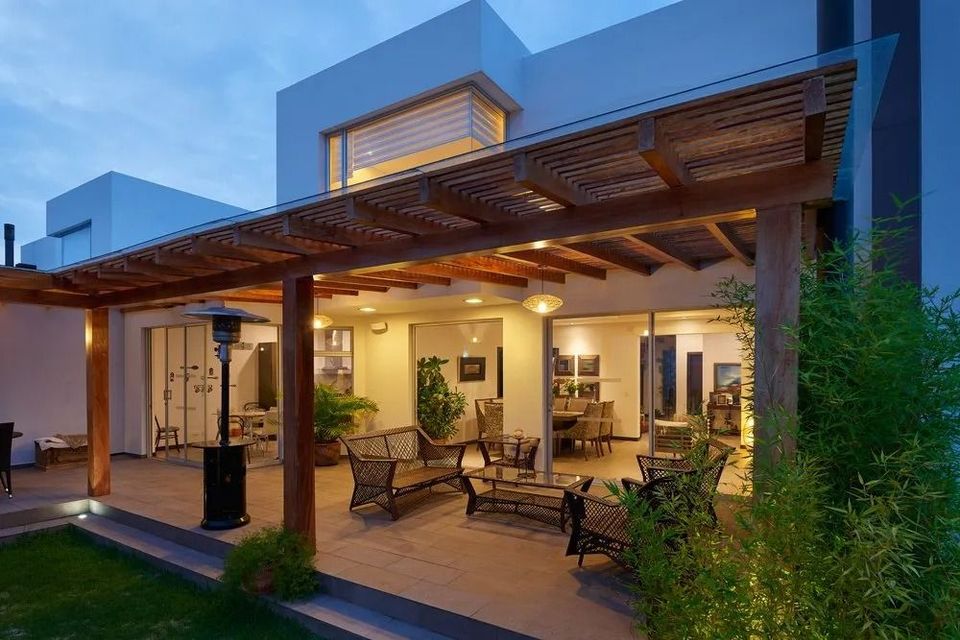 Modern house patio at dusk with warm lighting, lounge chairs, and an outdoor dining area