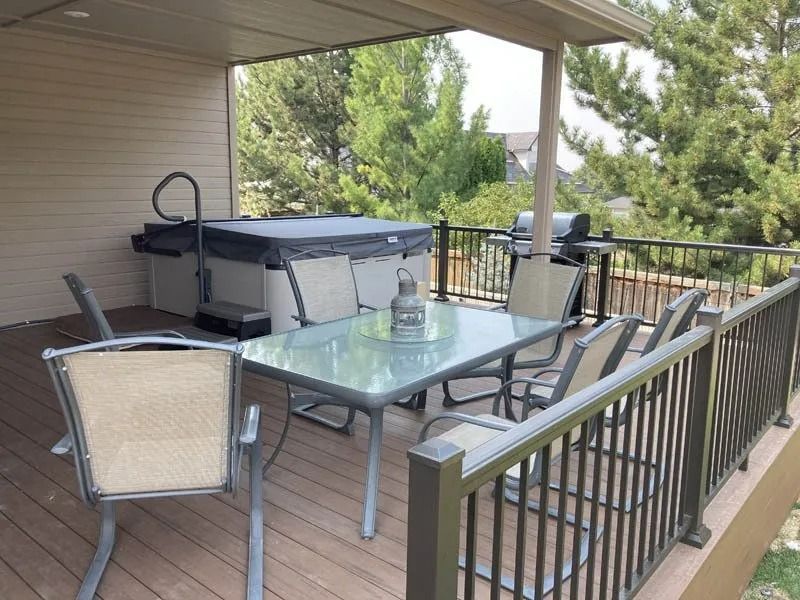Patio with glass table, chairs, and grill overlooking trees from a covered deck