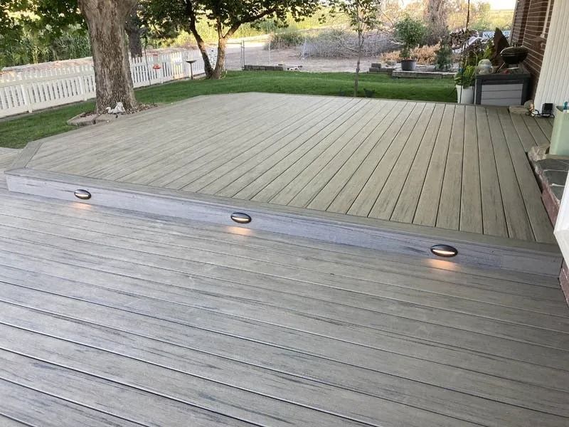 Wooden backyard deck with built-in lights, bordered by grass and trees