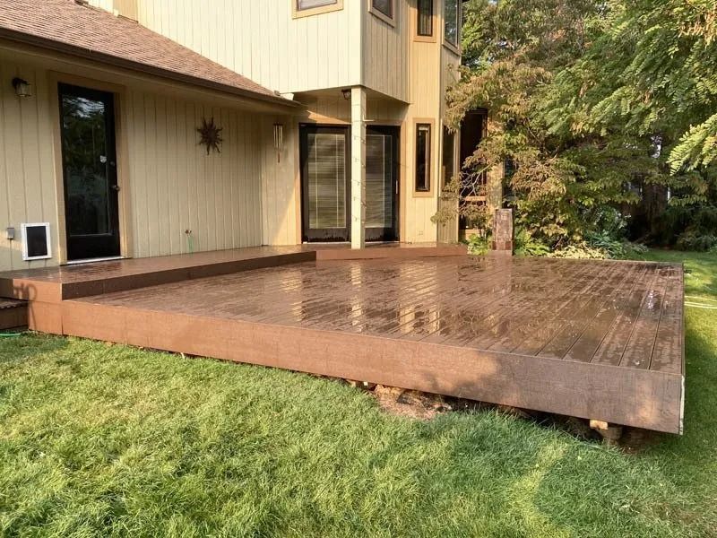 Back patio deck with wet reddish-brown tiles beside a tan house and green lawn