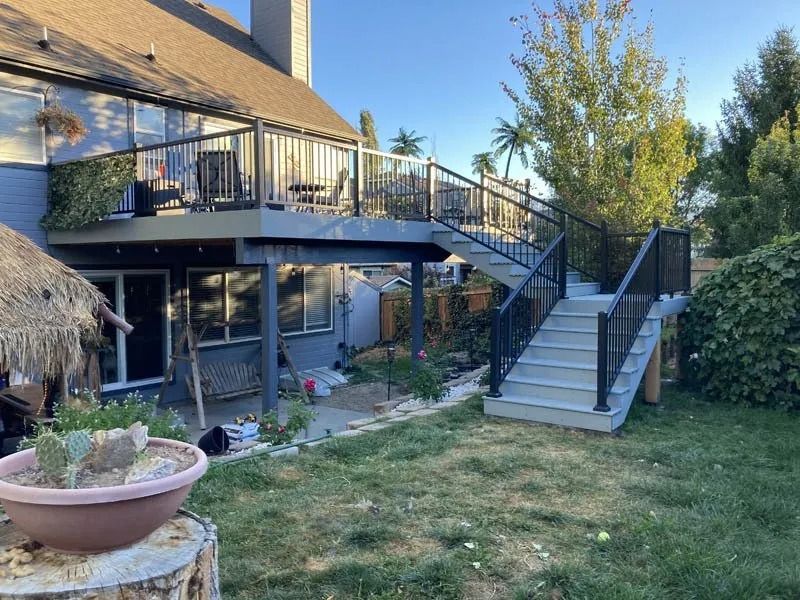Backyard patio with raised deck, black metal stairs, and sliding glass doors beside a grassy lawn