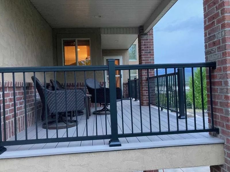 Covered porch with black railing, patio chairs, and a table beside a brick house.