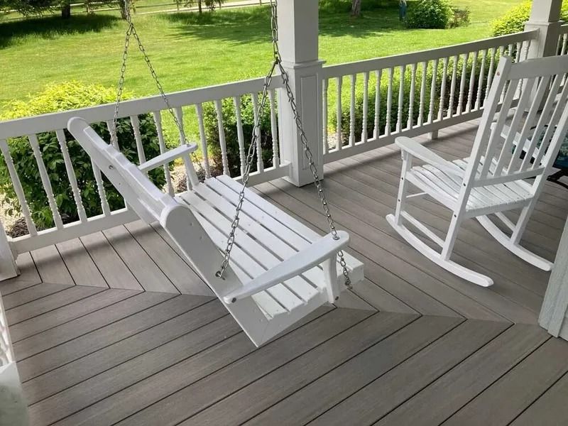 White wooden rocking chairs on a gray porch overlooking a green yard.