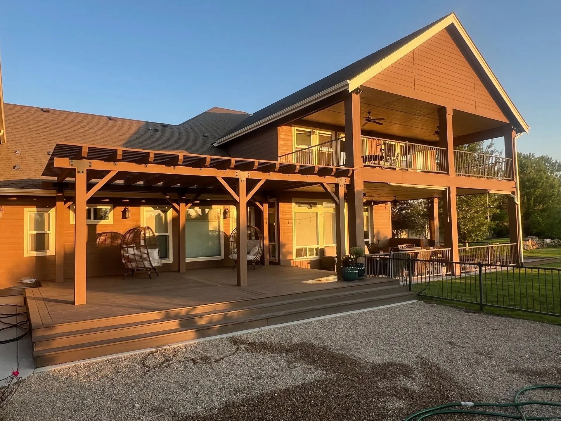 Sunlit modern lodge with a wraparound porch, wooden beams, and gravel driveway at sunset