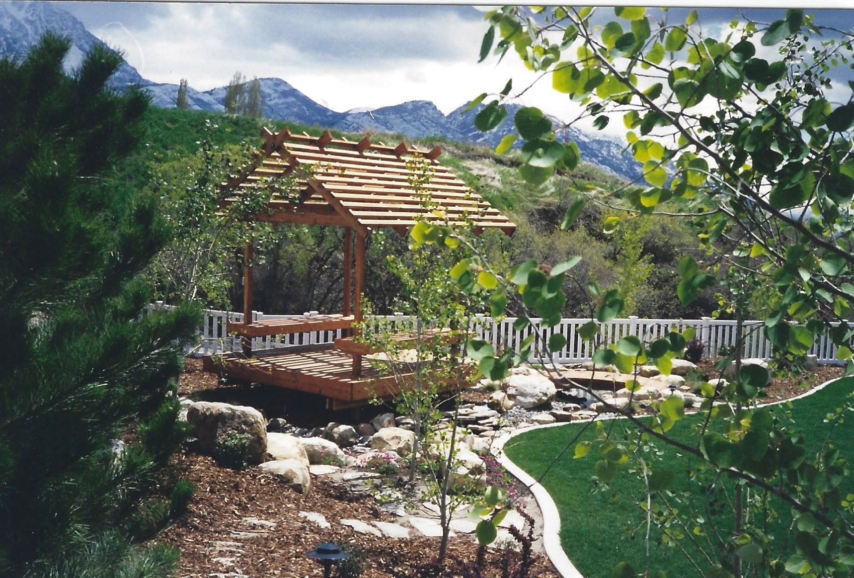 Garden gazebo with wooden deck, stone path, and mountain view surrounded by greenery