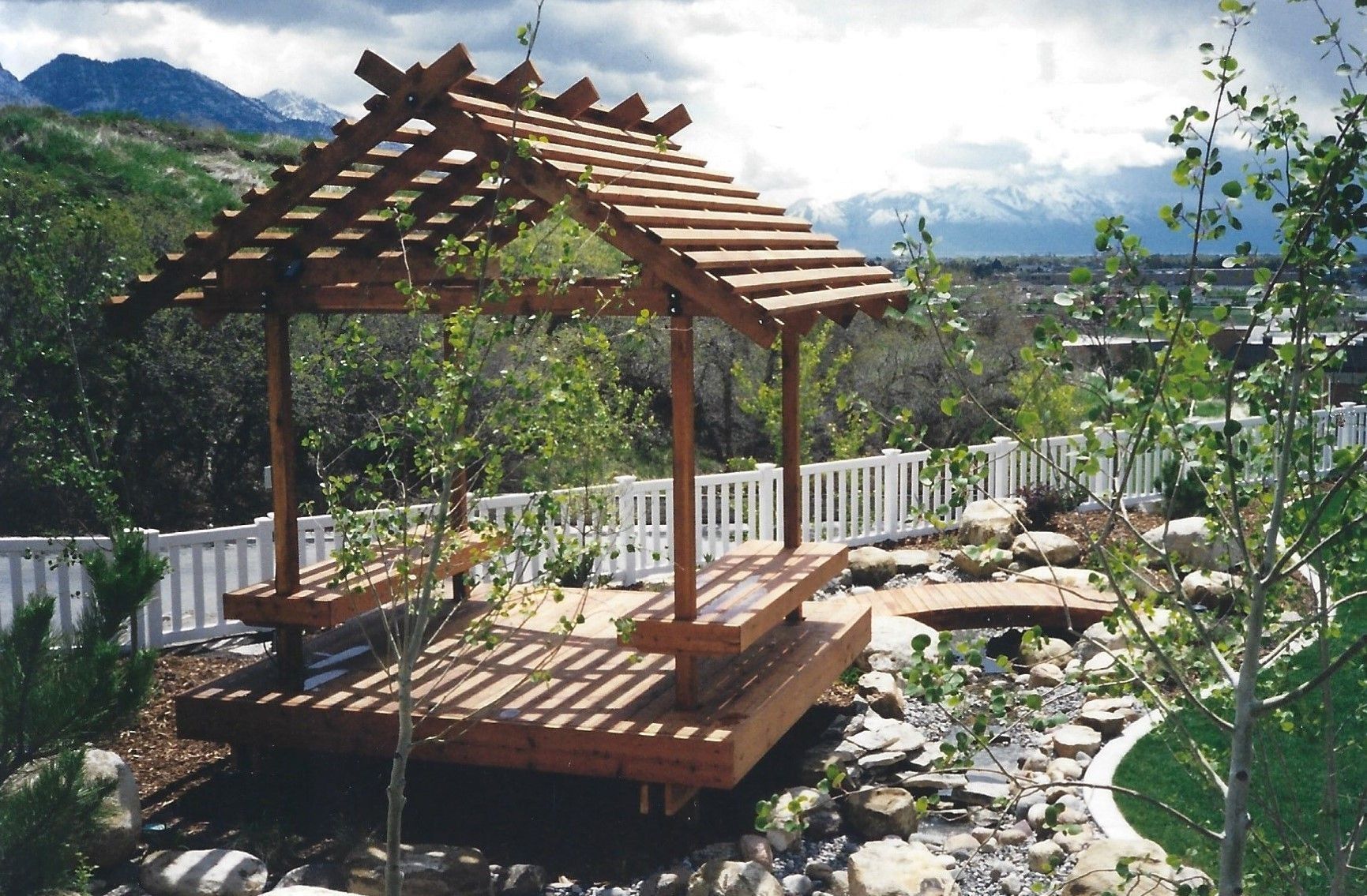 Wooden gazebo in a garden with mountain views, surrounded by greenery and a stone path