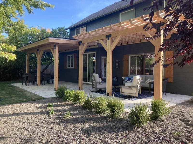 A large wooden pergola attached to a dark gray house over a patio with outdoor seating.