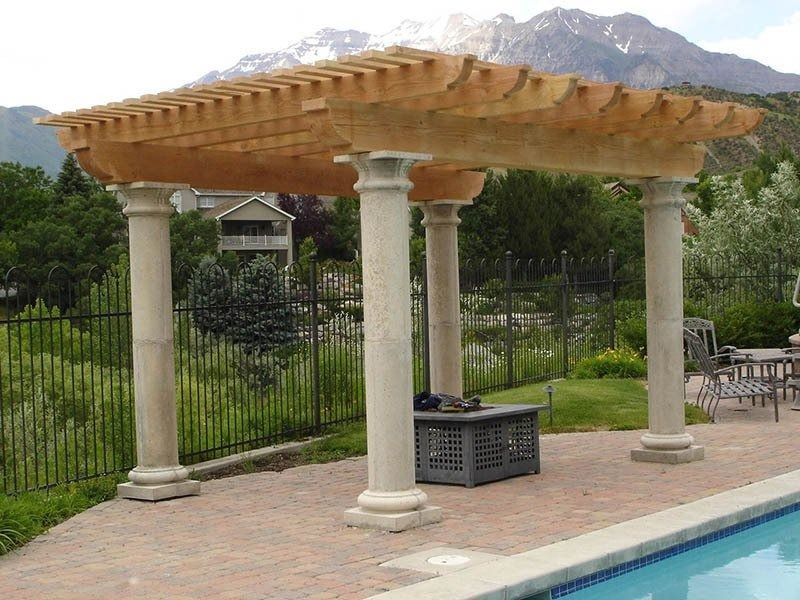 Poolside pergola with stone columns, wicker roof, and mountain view behind a fence