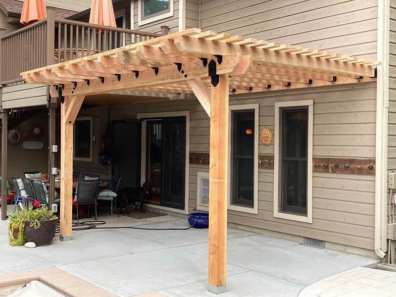 Backyard patio with wooden pergola over a concrete slab beside a house