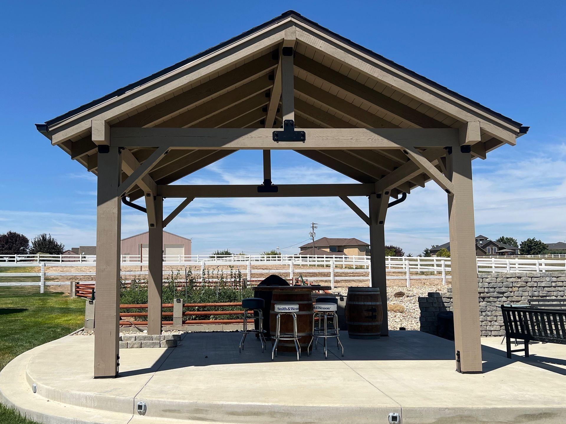Wooden outdoor pavilion with picnic tables on a concrete pad in a fenced open area