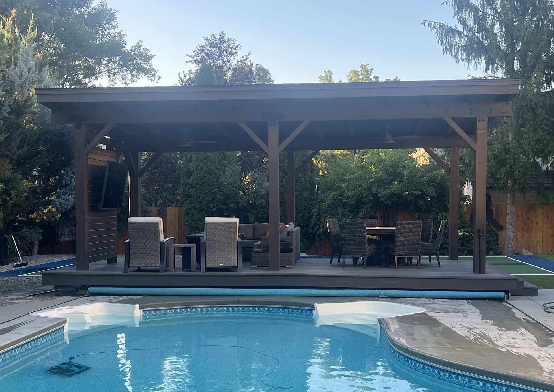 A covered deck with wicker furniture next to a swimming pool.