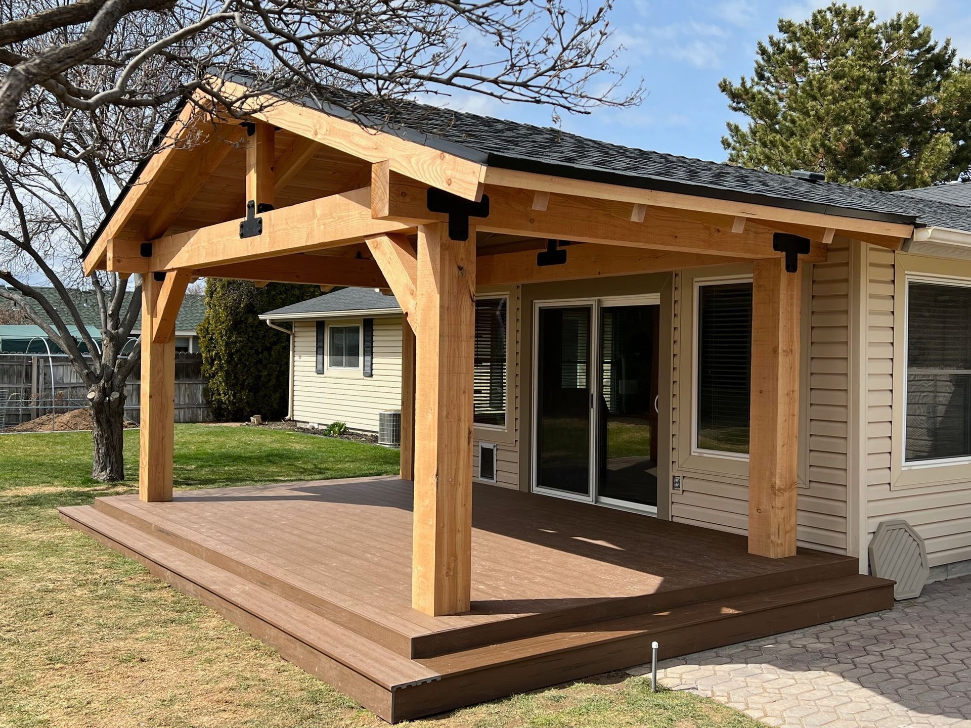 Small beige house with a wooden front porch and timber roof beams in a grassy yard