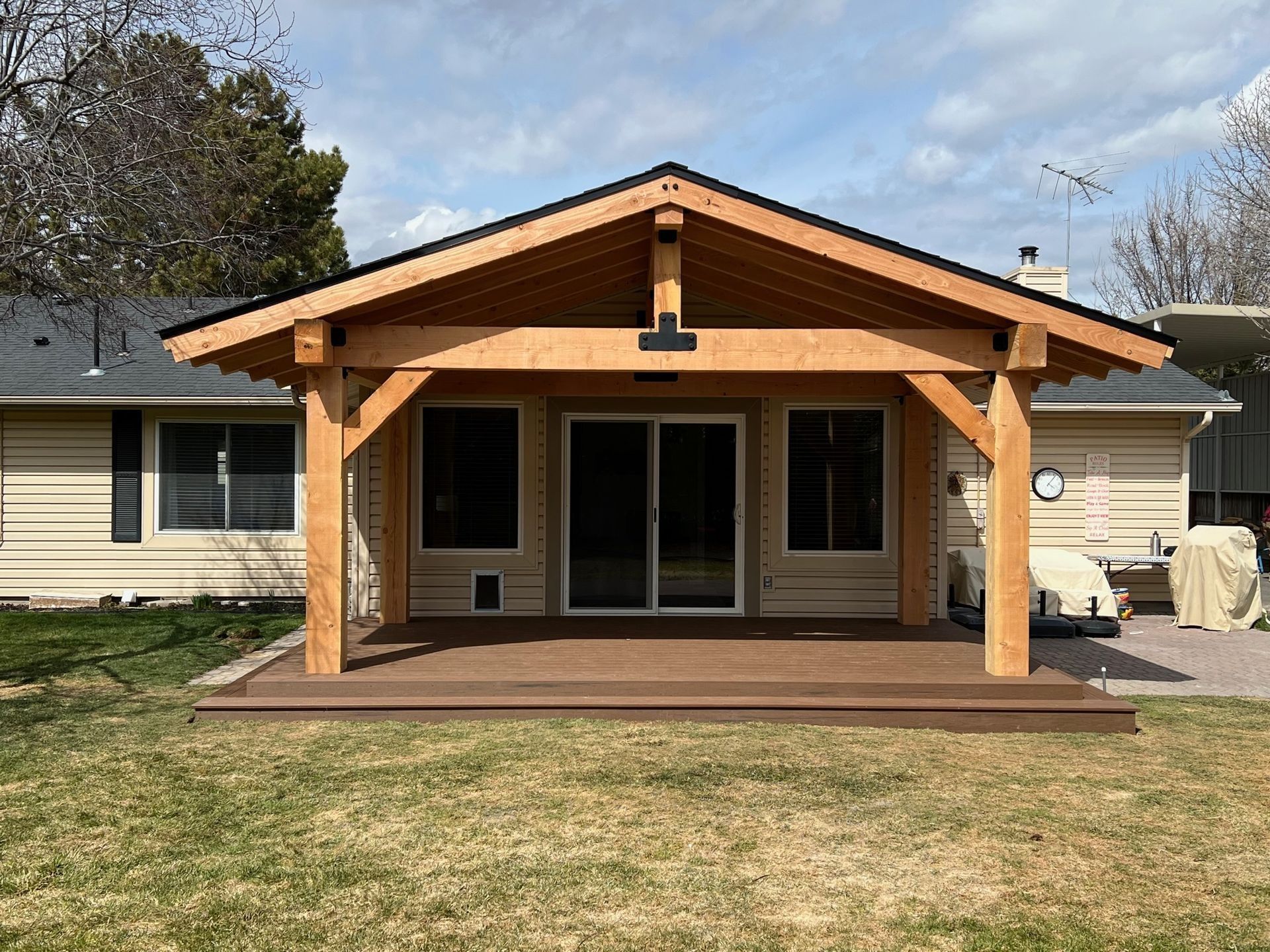 Wooden front porch with a gabled roof on a suburban house, viewed from the yard.