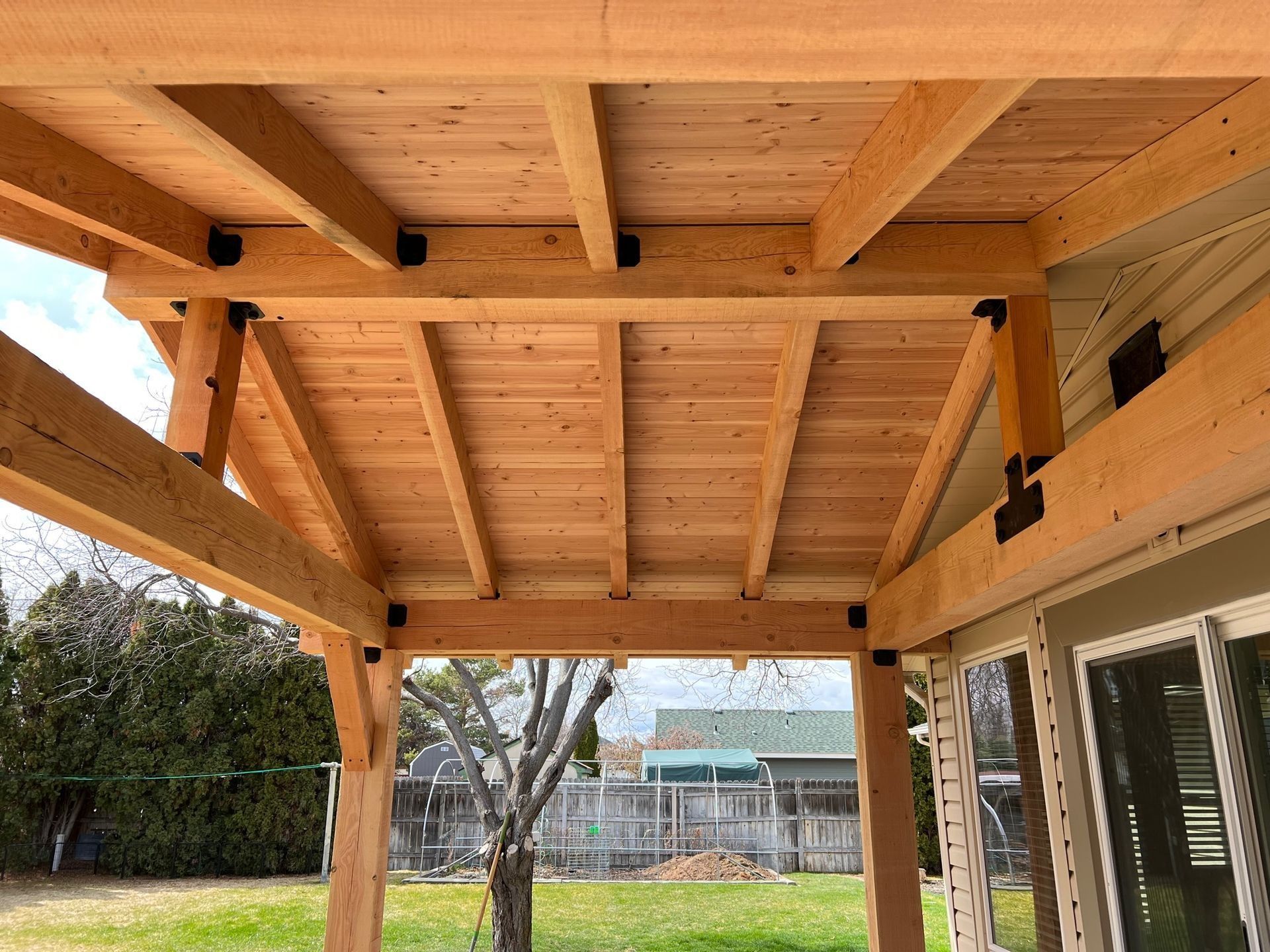 Wooden patio roof with exposed beams above a backyard and house windows