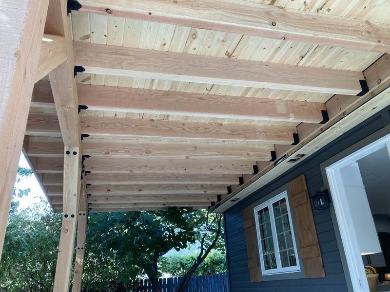 Wooden porch roof framing over a house exterior with exposed beams and posts