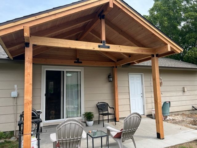 Covered patio with wood posts, ceiling fans, and seating outside a beige house