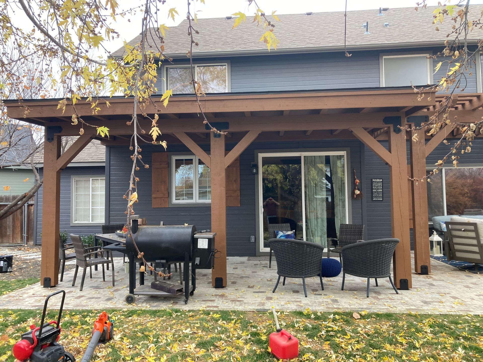 Backyard patio with wooden pergola, outdoor seating, grill, and sliding glass doors on a house